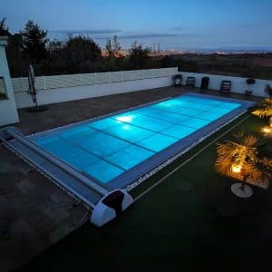 Couverture Eden partiellement déployée sur une piscine éclairée de nuit