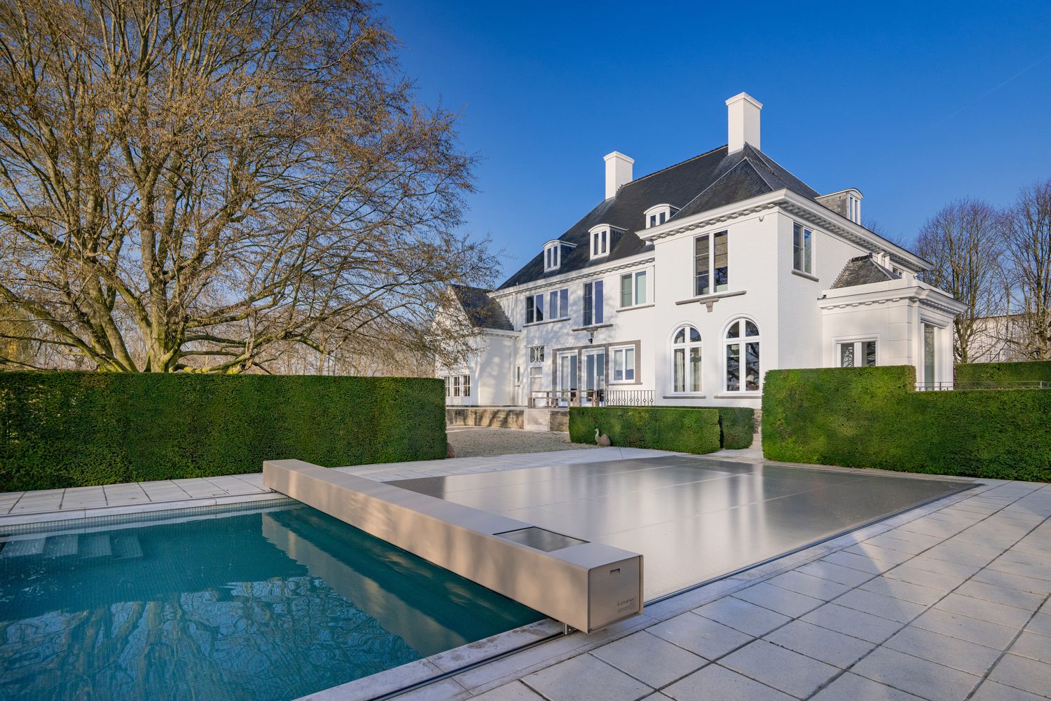 Couverture de piscine design déployée devant une demeure en pierre blanche